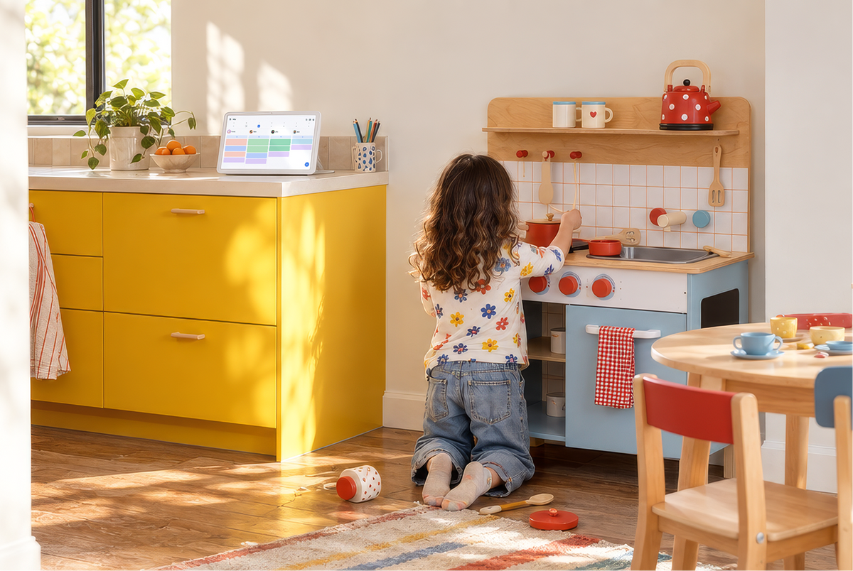 Home Hub on a yellow cabinet next to a play kitchen, showing the family calendar while a girl cooks up pretend tea